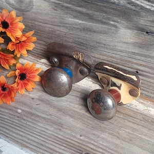 May include: Two antique door knobs with a weathered, metallic finish. One knob has a blue accent, the other has a cream and red accent. Orange flowers are arranged on a rustic, wooden surface.