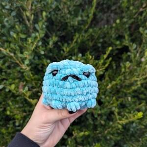 May include: A small, blue, crocheted plush toy shaped like a dog with black eyes and a black mustache.