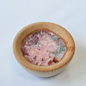 May include: A small wooden bowl filled with a pink and white mixture with glitter and small colorful pieces.