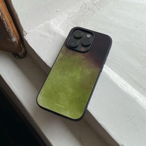 May include: A smartphone case featuring a gradient design that transitions from a deep black at the top to a vibrant olive green at the bottom. The case has a black frame and a triple-lens camera cutout. The word "olestone" is printed in small white text.