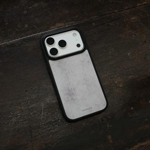 May include: A smartphone case with a black frame and a light gray, textured back panel featuring a mottled concrete-like appearance. The camera module area is white with three circular lens cutouts and a small flash opening. The word bluestone is printed.