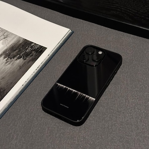 Può includere: Custodia per smartphone nera con finitura lucida. La custodia presenta un design orizzontale con un motivo bianco e nero. Il testo "NIGHT STUDIO" è stampato in basso. Un libro con una fotografia in bianco e nero è sullo sfondo.