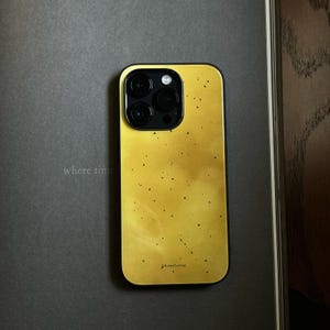 May include: A rectangular smartphone case with a vibrant yellow finish featuring a subtle, mottled texture and scattered dark speckles. The case includes a black camera module cutout with three circular lenses and the brand name pluestone printed.