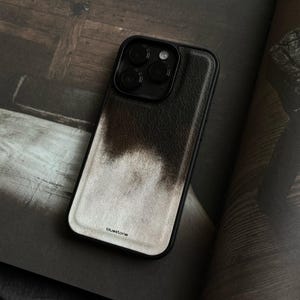 May include: A black smartphone case with a textured leather-like finish featuring a dark brown to light beige gradient fade. The case has a triple camera cutout at the top and the word bluestone printed in small black letters at the bottom.