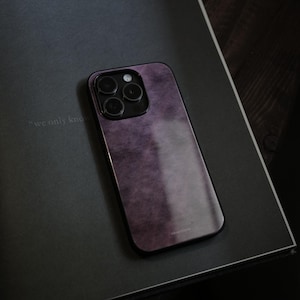 May include: Purple phone case with a textured finish, featuring a black camera module. The case is resting on a dark gray surface, with the phrase "we only know" subtly visible. The phone case has a sleek, modern design.