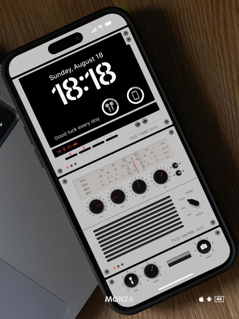 May include: A white smartphone with a black screen displaying a digital clock with the time 18:18 and the date Sunday, August 18. The text "Good luck every day" is displayed below the clock. The screen also shows a stylized image of a vintage radio with knobs and dials.