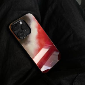Op de afbeelding: Een smartphonehoesje met een levendig abstract ontwerp in tinten rood, wit en bruin. De hoes heeft een glanzende afwerking en een zwart cameramodule. De merknaam "bluestone" staat rechtsonder gedrukt.