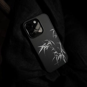 May include: A matte black smartphone case featuring a white line-art illustration of bamboo stalks and leaves. The case has a rectangular camera cutout with three circular lenses visible. The text "blueslone" is printed in small white letters.