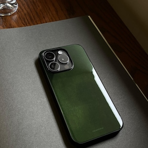 May include: A dark green phone case with a glossy finish, featuring a black camera module. The case is resting on a dark gray surface. The brand name "bluetone" is printed on the bottom of the case.