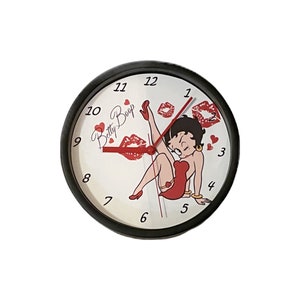 May include: A black and white clock with a red and white Betty Boop design. The clock features a cartoon image of Betty Boop with red lips and a red dress. The clock face has black numbers and a red hour hand.