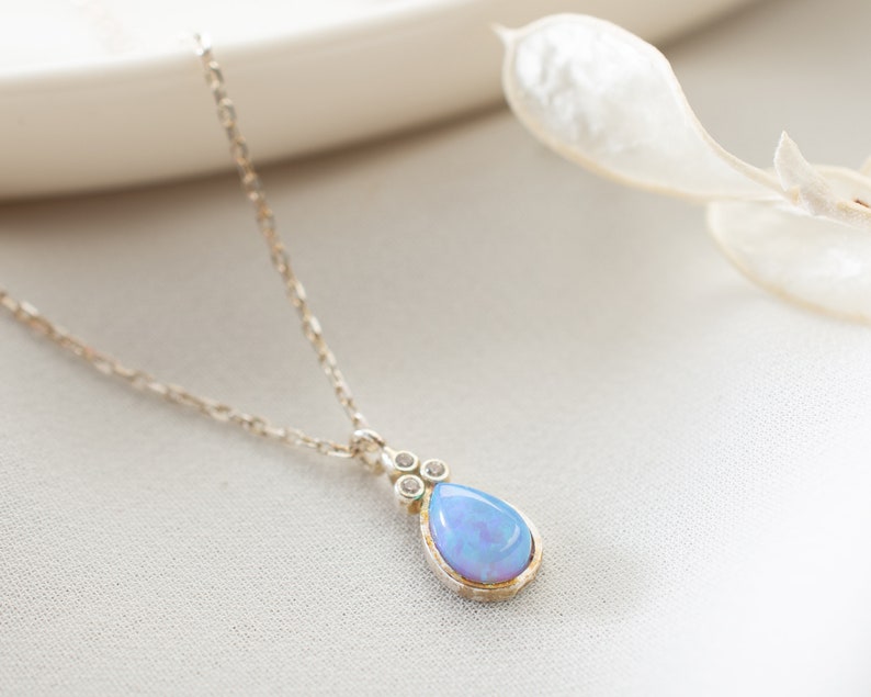 Puede incluir: Un delicado collar de cadena de plata con un colgante de &oacute;palo en forma de l&aacute;grima acentuado con peque&ntilde;as piedras transparentes.