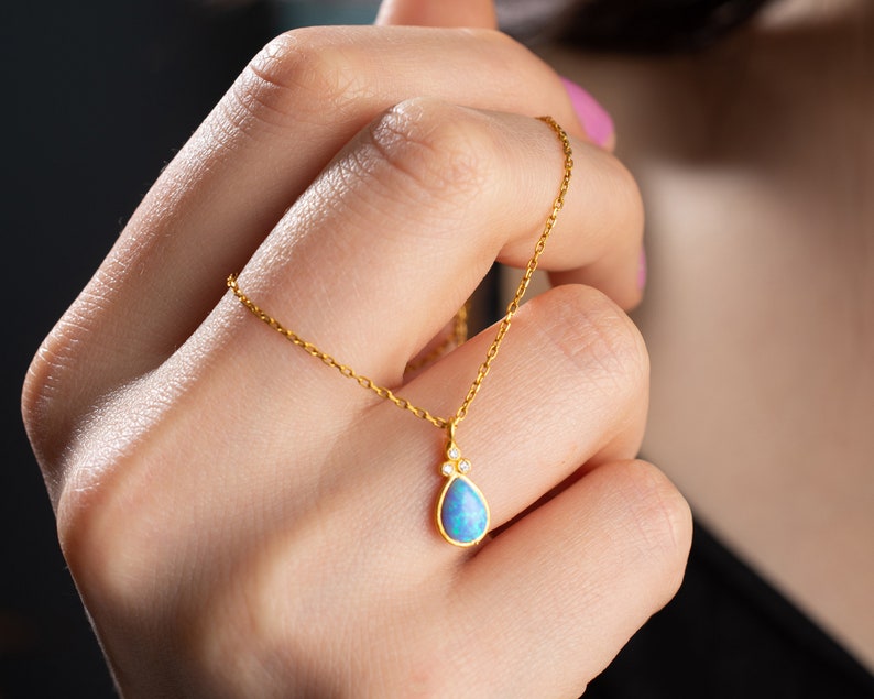 Puede incluir: Un delicado collar de cadena de oro con un colgante en forma de l&aacute;grima que presenta una piedra de &oacute;palo azul y peque&ntilde;as piedras preciosas transparentes.