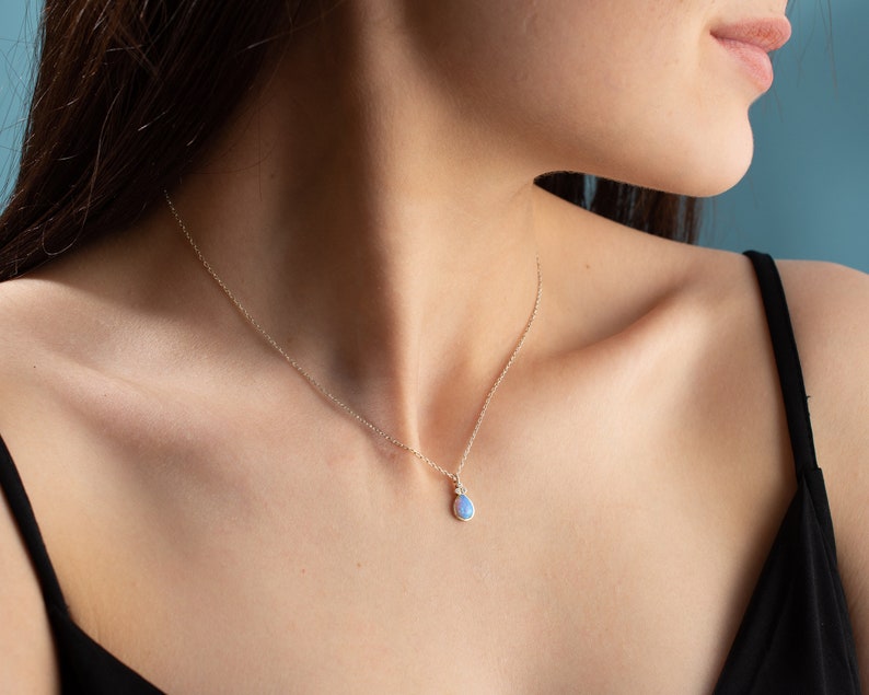 Puede incluir: Un collar de cadena de plata con un colgante en forma de l&aacute;grima con una piedra de &oacute;palo azul claro.