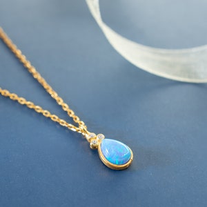 Puede incluir: Un delicado collar de cadena de oro con un colgante de &oacute;palo azul en forma de l&aacute;grima acentuado con peque&ntilde;as piedras preciosas transparentes.