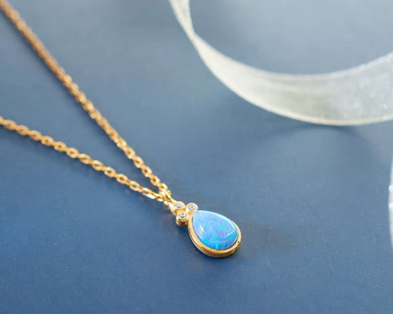 Puede incluir: Un delicado collar de cadena de oro con un colgante de &oacute;palo azul en forma de l&aacute;grima acentuado con peque&ntilde;as piedras preciosas transparentes.