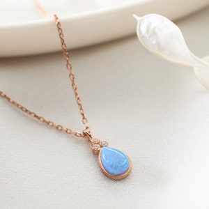 Puede incluir: Un delicado collar de oro rosa con un colgante de opalo azul en forma de l&aacute;grima adornado con peque&ntilde;as piedras transparentes.
