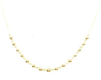 Op de afbeelding: Een gouden ketting met een delicate ketting en kleine ronde kralen.
