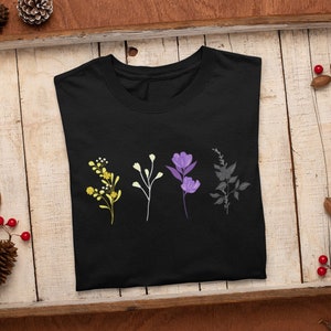 May include: Black t-shirt with a design of four stylized flowers in yellow, white, purple, and gray. The flowers are arranged vertically in a row.