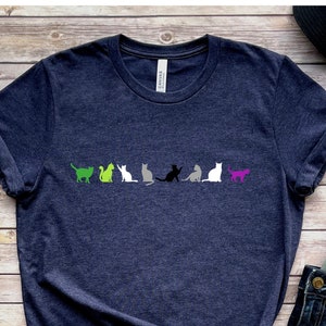 以下が含まれることがあります： ヘザーネイビーのTシャツに、無性愛のプライドフラッグを表す、さまざまな色の猫が7匹並んでいます。