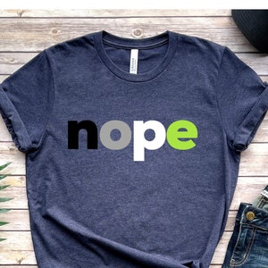 May include: A heather navy blue t-shirt with the word "nope" printed in black, gray, and green letters.
