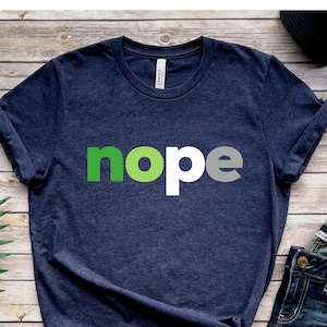 Puede incluir: Una camiseta azul marino jaspeada con la palabra "nope" impresa en letras verdes y blancas.