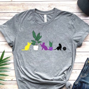 May include: A gray t-shirt with a graphic of four cats and plants. The cats are yellow, purple, and black. The text "ATHLETIC HEATHER" is printed below the graphic.