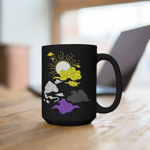 Puede incluir: Taza de cerámica negra con un diseño de sol y nubes en amarillo, blanco, gris y morado. Las nubes están estilizadas y se asemejan a los colores de la bandera del orgullo no binario.