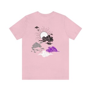 以下が含まれることがあります： 黒、白、グレー、紫の太陽と雲のグラフィックが描かれたピンクのTシャツです。