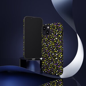 May include: Two black smartphones, one with a patterned case and one without. The case features a black background with a repeating pattern of yellow, purple, and white irregular shapes. The phones are displayed on a dark blue surface.