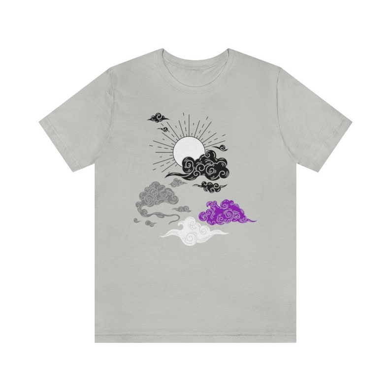 以下が含まれることがあります： 黒と白の太陽と雲のデザインが施されたグレーのTシャツ。雲はアセクシュアルプライドフラッグの色、黒、グレー、白、紫です。