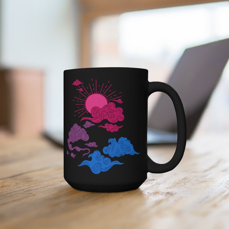 May include: A black ceramic mug with a bi-pride flag inspired design. The design features a pink and blue sun with clouds in the sky.