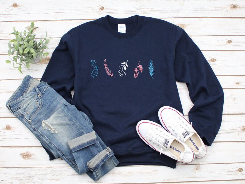 May include: A navy blue sweatshirt with a white, pink, and blue floral design on the front. The sweatshirt is paired with blue jeans and white sneakers.