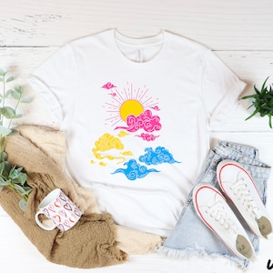 May include: White t-shirt with a graphic of a sun with rays and clouds in pink, blue, and yellow colors. The graphic is reminiscent of a pride flag.
