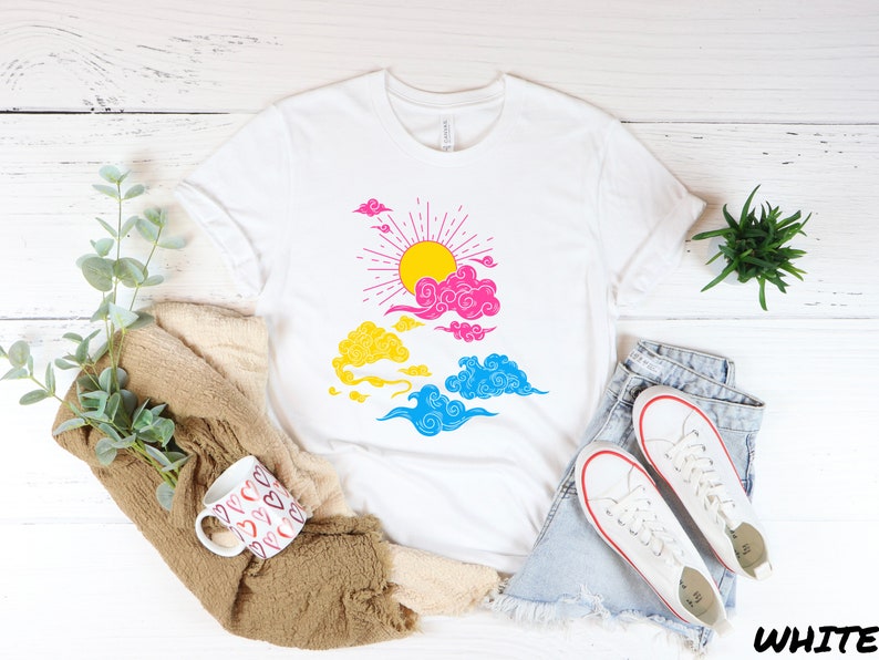 May include: White t-shirt with a graphic of a sun with rays and clouds in pink, blue, and yellow colors. The graphic is reminiscent of a pride flag.