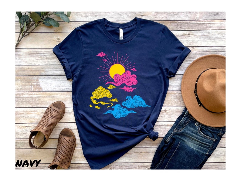 May include: A navy blue t-shirt with a graphic of a sun and clouds in pink, yellow, and blue. The clouds are stylized and have a whimsical look.