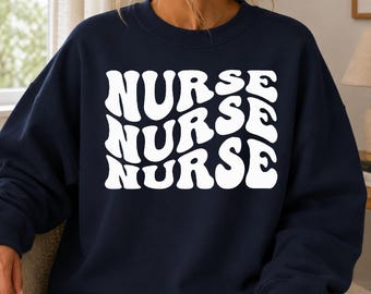 Könnte beinhalten: Ein marineblaues Sweatshirt mit Rundhalsausschnitt und dem Wort NURSE, das dreimal in einer gestapelten, weißen, wellenförmigen Schrift im Retro-Stil auf der Brust gedruckt ist. Das Kleidungsstück hat lange Ärmel mit gerippten Bündchen.