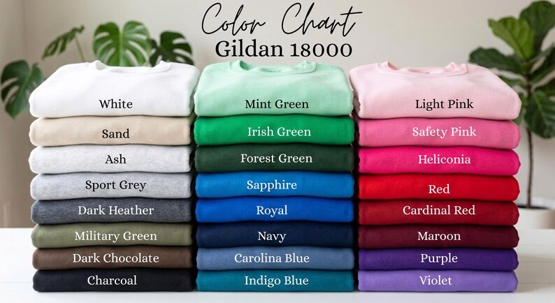 May include: A color chart for Gildan 18000 sweatshirts featuring three vertical stacks of folded garments in various colors. The text reads Color Chart Gildan 18000, with labels for each color including White, Sand, Ash, Sport Grey, Dark Heather, Military Green, Dark Chocolate, Charcoal, Mint Green, Irish Green, Forest Green, Sapphire, Royal, Navy, Carolina Blue, Indigo Blue, Light Pink, Safety Pink, Heliconia, Red, Cardinal Red, Maroon, Purple, and Violet.