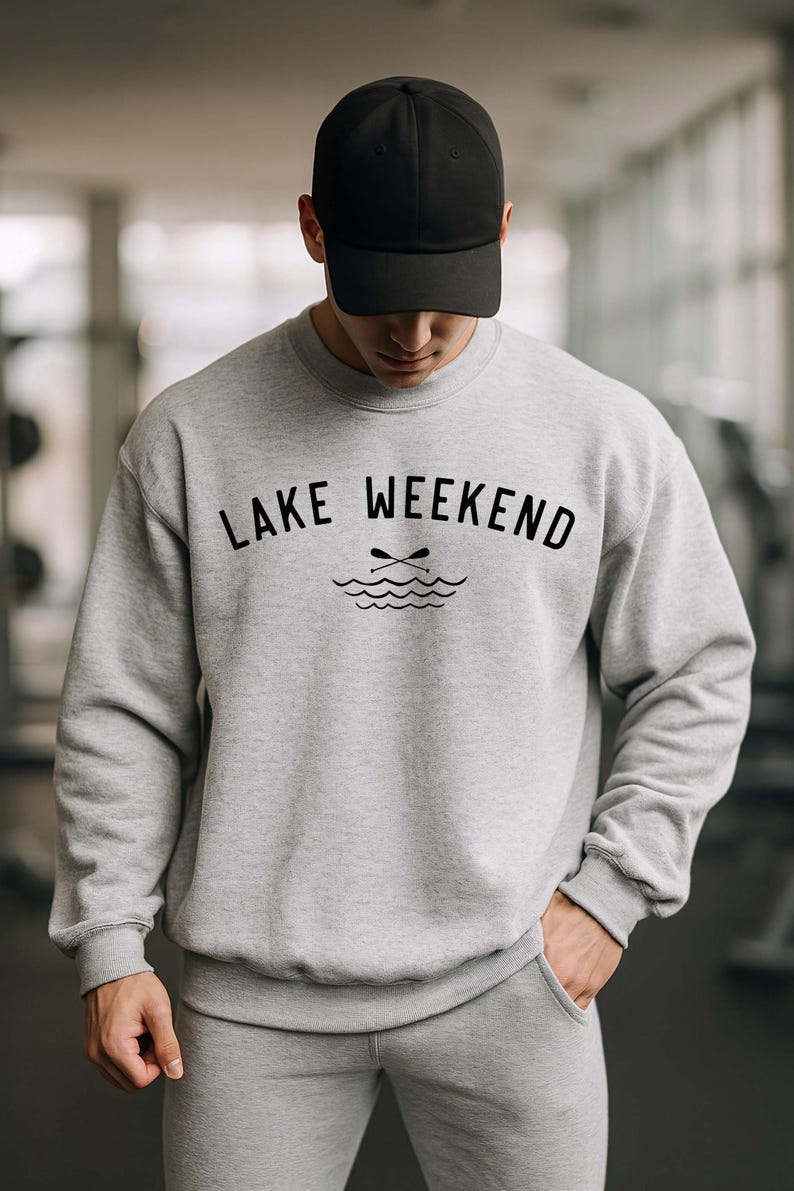 May include: A light gray crewneck sweatshirt featuring the black text LAKE WEEKEND and a graphic of two crossed oars above wavy lines, paired with a matching light gray baseball cap. The sweatshirt has long sleeves and a ribbed hem and cuffs.