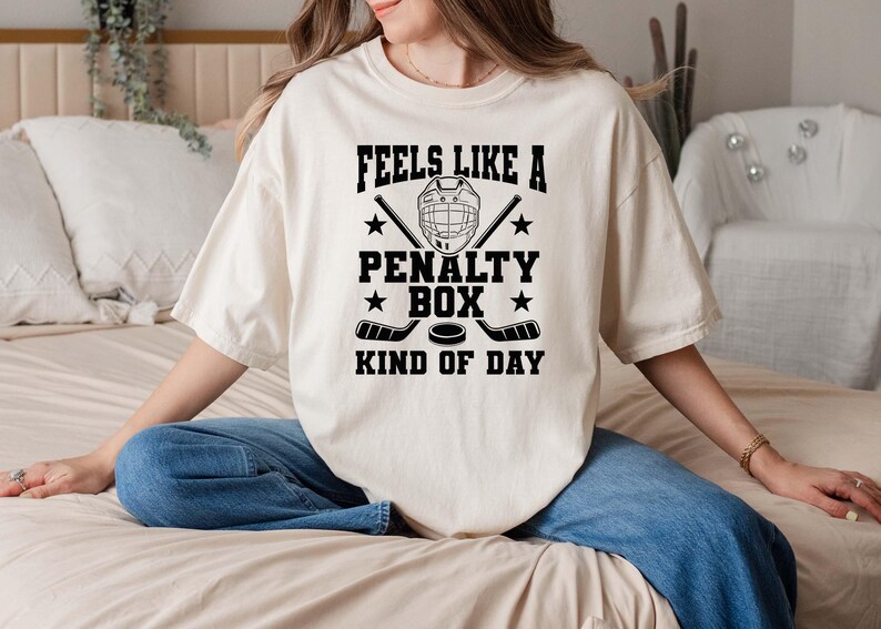 A woman wearing a white t-shirt with a humorous text printed on it, sitting on a bed.