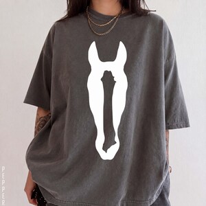 K&ouml;nnte beinhalten: Ein anthrazitfarbenes Kurzarm-T-Shirt mit einer gro&szlig;en, einfarbig wei&szlig;en Grafik einer Pferdekopf-Silhouette in der Mitte der Brust. Das Shirt hat einen Rundhalsausschnitt und einen lockeren Schnitt mit &uuml;berschnittenen Schultern und Stoff.