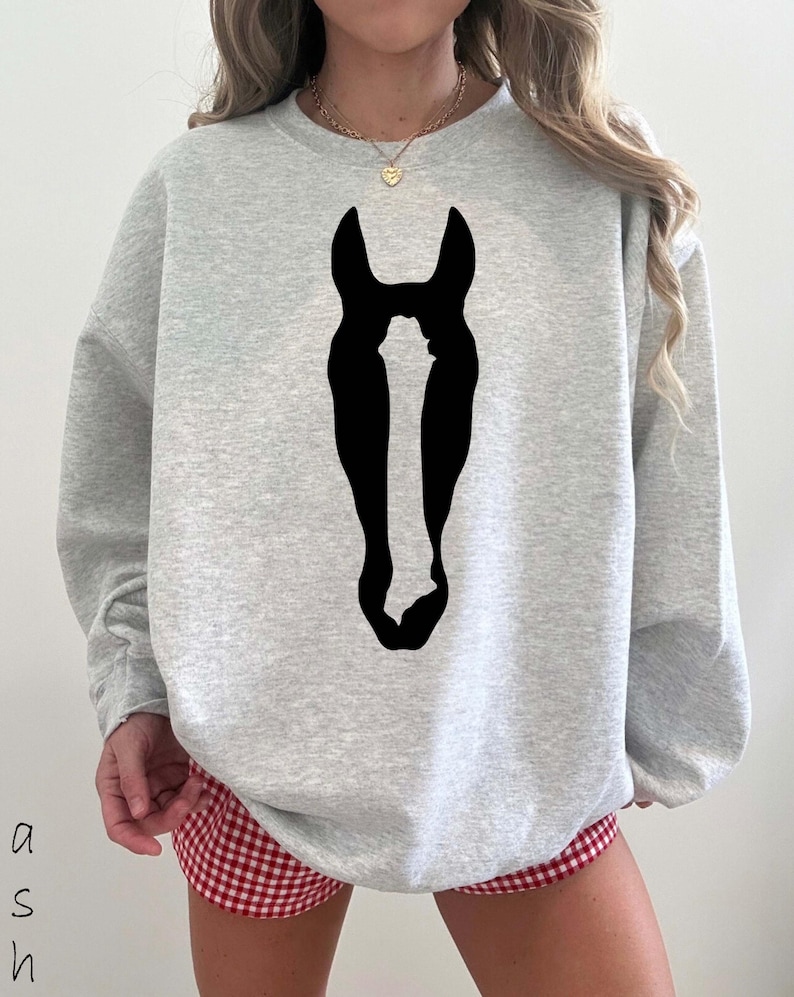 K&ouml;nnte beinhalten: Ein hellgraues Sweatshirt mit Rundhalsausschnitt und einer gro&szlig;en, einfarbig schwarzen Silhouette eines Pferdekopfes in der Mitte der Brust. Das Kleidungsst&uuml;ck hat lange &Auml;rmel und einen gerippten Ausschnitt f&uuml;r einen schlichten Look.