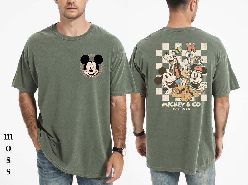 Op de afbeelding: Mosgroen t-shirt met Mickey Mouse op de voorkant en een groep Disney-personages op de achterkant. Het shirt heeft een klassieke pasvorm en is gemaakt van een zacht, comfortabel materiaal. De achterkant van het shirt heeft Mickey & Co. Est. 1928.