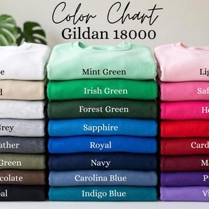 K&ouml;nnte beinhalten: Eine Farbkarte f&uuml;r Gildan 18000 Sweatshirts mit drei vertikalen Stapeln gefalteter Kleidungsst&uuml;cke in verschiedenen Farben. Der Text lautet Color Chart Gildan 18000, mit Beschriftungen f&uuml;r jede Farbe, darunter White, Sand, Ash, Sport Grey, Dark Heather, Military Green, Dark Chocolate, Charcoal, Mint Green, Irish Green, Forest Green, Sapphire, Royal, Navy, Carolina Blue, Indigo Blue, Light Pink, Safety Pink, Heliconia, Red, Cardinal Red, Maroon, Purple und Violet.