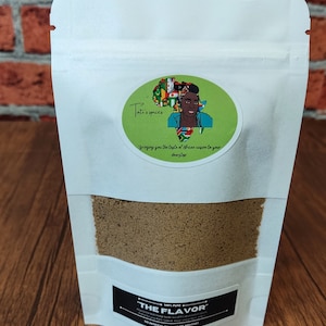 Könnte beinhalten: Ein weißer wiederverschließbarer Beutel mit einem grünen runden Aufkleber, der eine Comic-Illustration einer Frau mit einer Karte des afrikanischen Kontinents dahinter zeigt. Der Text auf dem Aufkleber lautet "Tati's spices" und "Bringing you the taste of African cuisine to your doorstep". Der Beutel enthält eine braune Gewürzmischung und ein schwarzes Etikett mit der Aufschrift "100% PURE THE FLAVOR" und "Alles natürliche Gewürzmischung aus den feinsten und aromatischsten Gewürzen für Ihr BBQ, Gegrilltes, Topf und viele weitere Gerichte. OHNE KÜNSTLICHE FARBSTOFFE ODER ZUSATZSTOFFE."