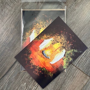 K&ouml;nnte beinhalten: Drei wei&szlig;e Geister versammeln sich um ein Lagerfeuer in einer dunklen Waldkulisse. Die Geister sind in einem verspielten Stil mit leuchtenden Augen und einem warmen orangenen Schein vom Feuer gemalt.
