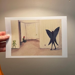 May include: A rectangular art print featuring a surreal illustration of a dark, winged creature with glowing red eyes standing in a beige room. A small green figure stands to the left, while a figure with a red head sits in the background.