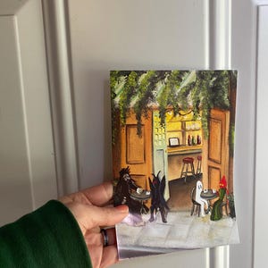K&ouml;nnte beinhalten: Ein Gem&auml;lde, das eine Caf&eacute;szene mit drei Figuren zeigt, die an Tischen sitzen. Die Figuren sind ein schwarzes Monster, ein wei&szlig;es Gespenst und ein rotes Monster. Das Caf&eacute; ist mit gr&uuml;nen Ranken geschm&uuml;ckt und hat ein gelbes Interieur.