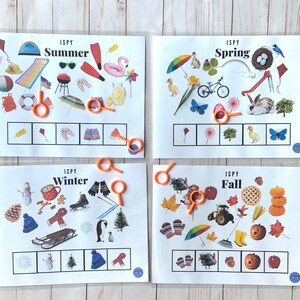 May include: Four printable I Spy game cards featuring different seasons: Summer, Spring, Winter, and Fall. Each card has a grid of squares with magnifying glasses and a list of items to find within the image.