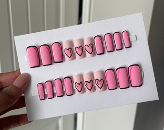 May include: A set of ten pink press-on nails with black outlines.  Five nails have a pink heart design.