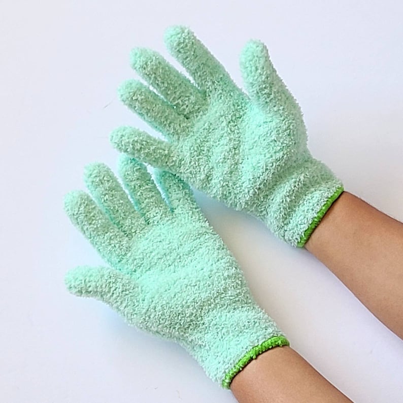 May include: A pair of light green microfiber cleaning gloves with green trim. The gloves are worn on a person's hands.